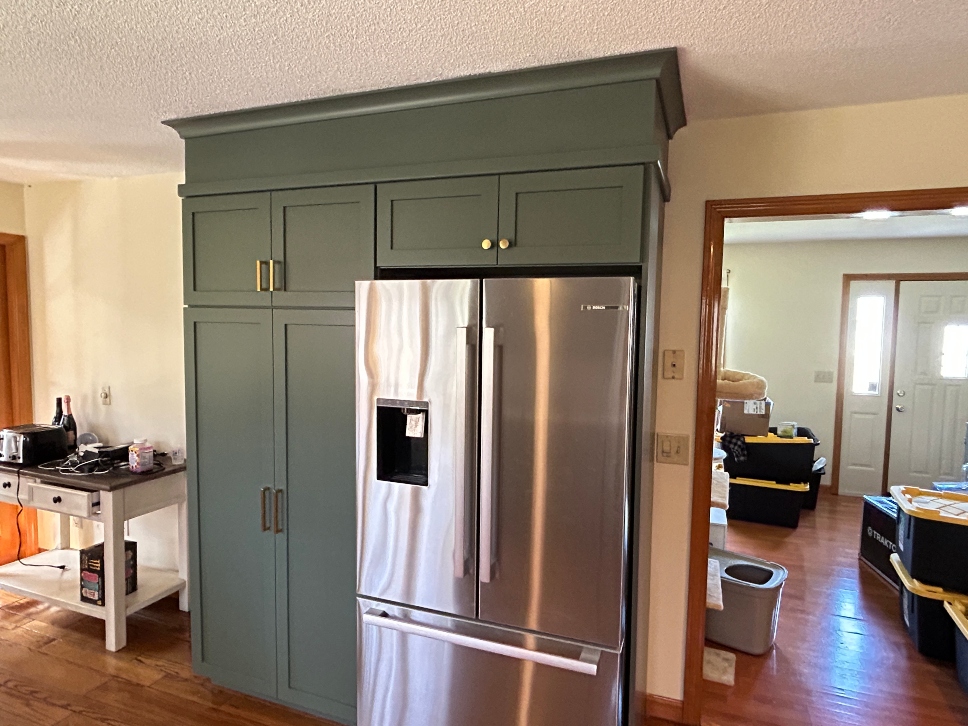 Adding storage cabinets in Chicopee MA — new green shaker upper cabinets with crown molding and gold hardware matching existing kitchen style