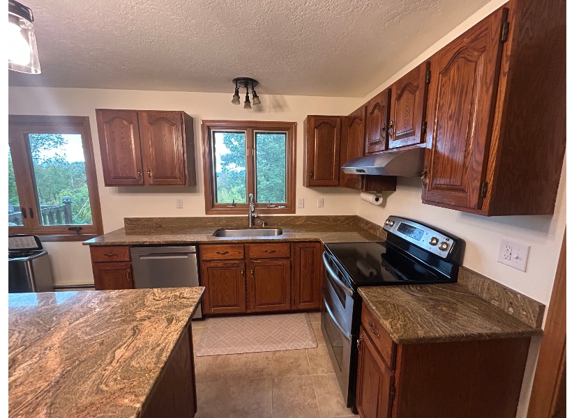 Before cabinet refacing in Belchertown MA — dated dark oak cathedral-style wall cabinets with brass hardware and granite countertops