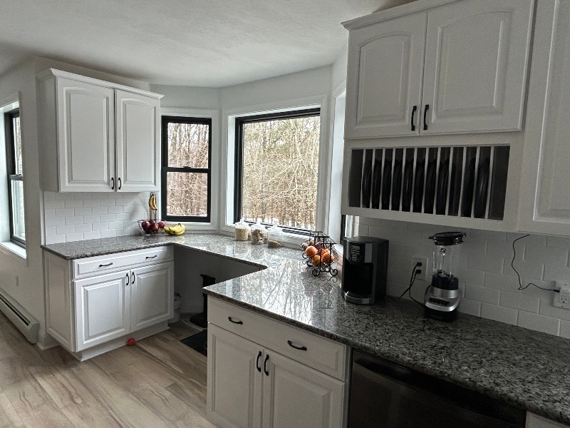 White cabinet painting with raised-panel doors, granite countertops, bay window, and built-in plate rack